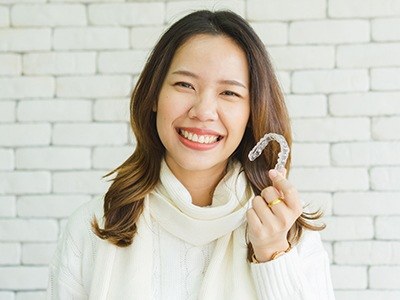 Woman in white sweater smiling and holding Invisalign aligner