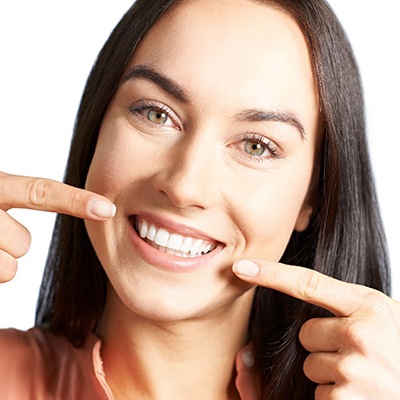 Woman pointing to her smile after correcting crowded teeth with Invisalign in Fort Worth