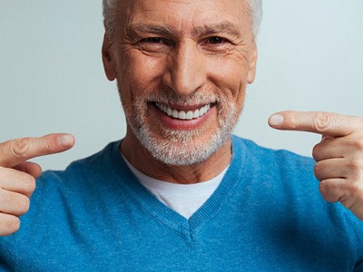 Older man in blue shirt pointing to his smile with his pointer fingers