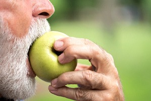 Nose-to-chin profile view of a man with a white beard biting into a green apple