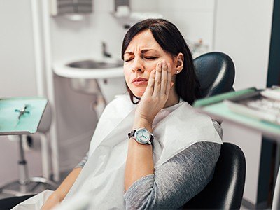 A distraught woman rubbing her cheek while sitting in dental chair