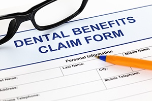 Top portion of a dental benefits claim form with a pen and black framed glasses