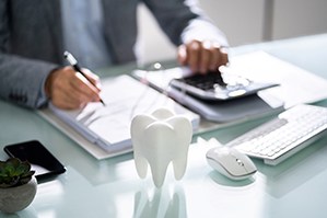 Man at desk with papers, keyboard, calculator, and large model tooth