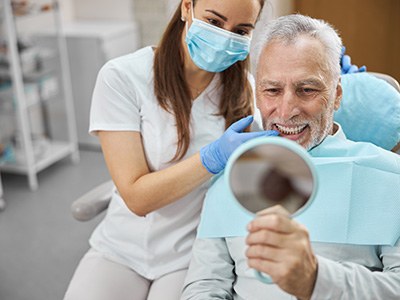 An older man admiring his new dental implant in a hand mirror