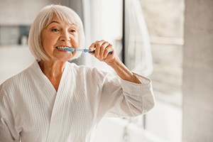 An older woman brushing her teeth in front of a bathroom mirror