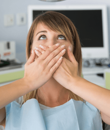 Woman in dental chair covering mouth with both hands