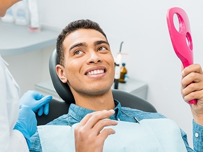 Dental patient looking at his smile in pink mirror