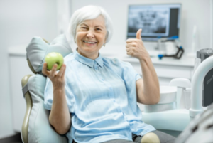 Woman with dental implants smiling and holding an apple after treatment